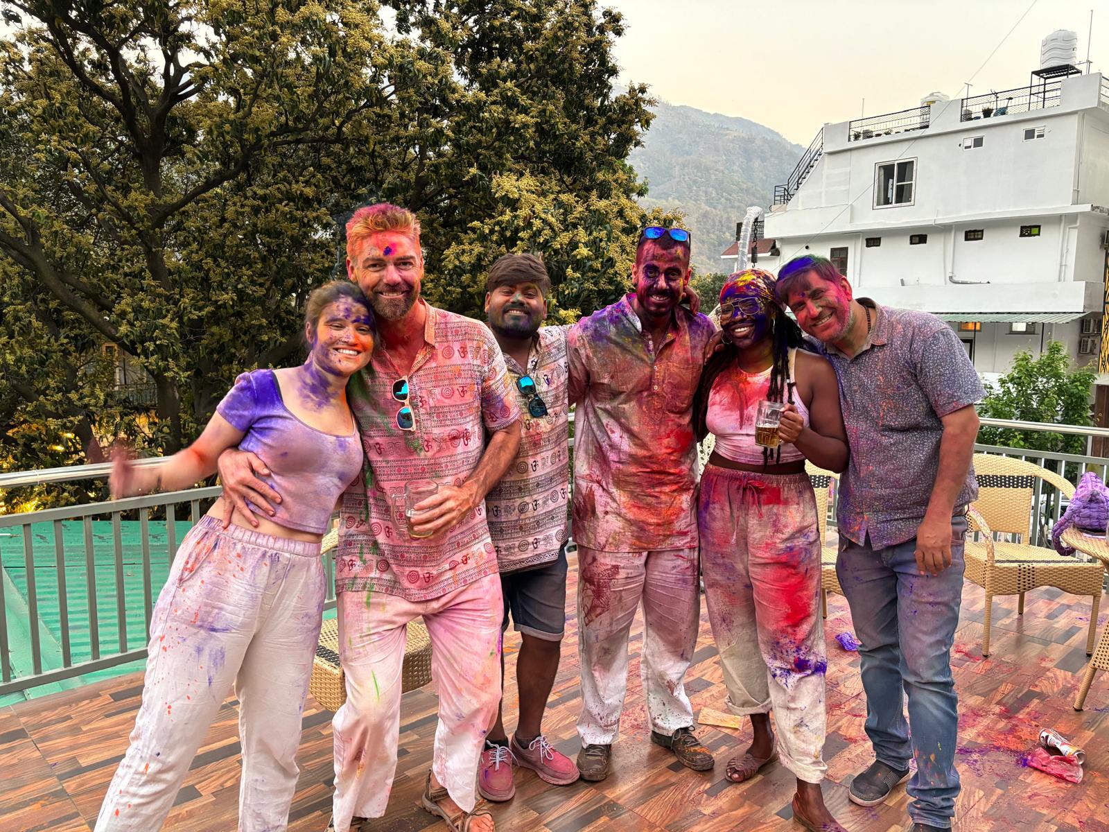 Grupo celebrando Holi, cubiertos de colores brillantes en una terraza al aire libre.