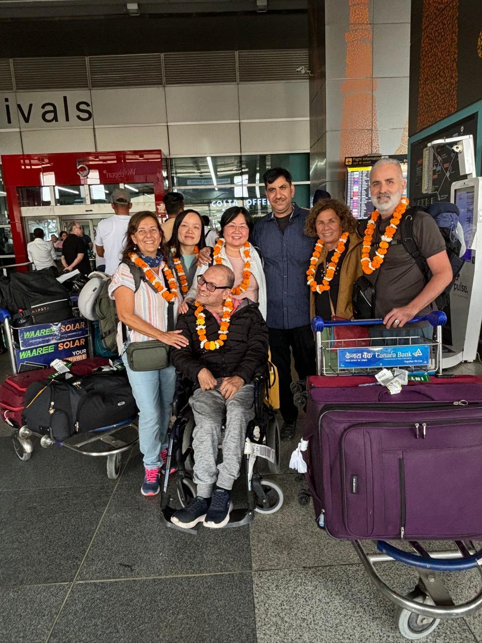 Grupo de viajeros en India con maletas y guirnaldas en un aeropuerto.