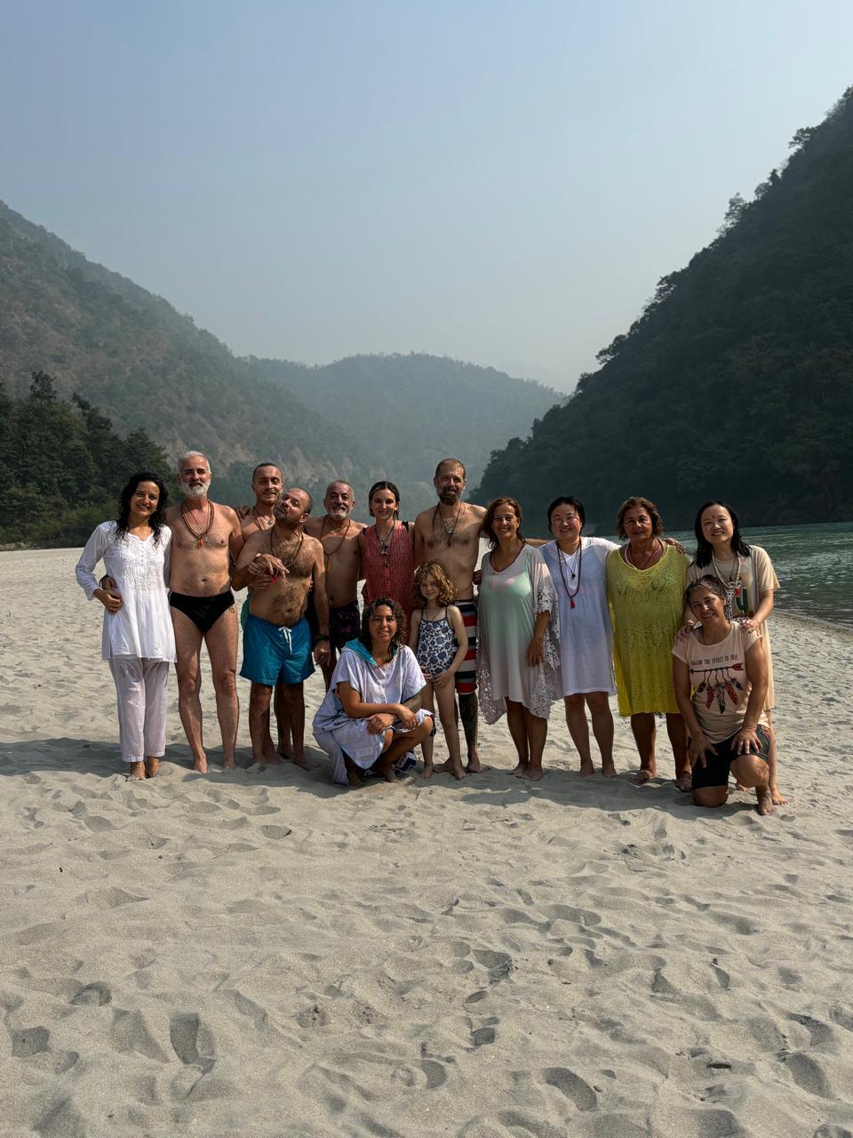 Grupo de turistas posando en la playa junto al río, rodeados de montañas.