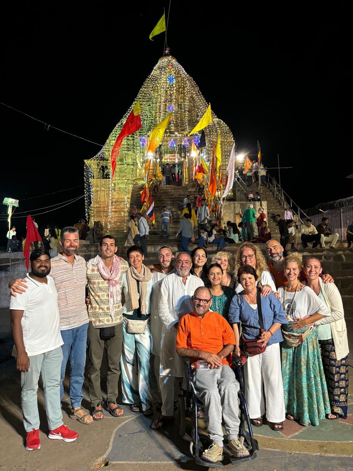 Un grupo de viajeros sonríe frente a un templo iluminado con luces y banderas en India.