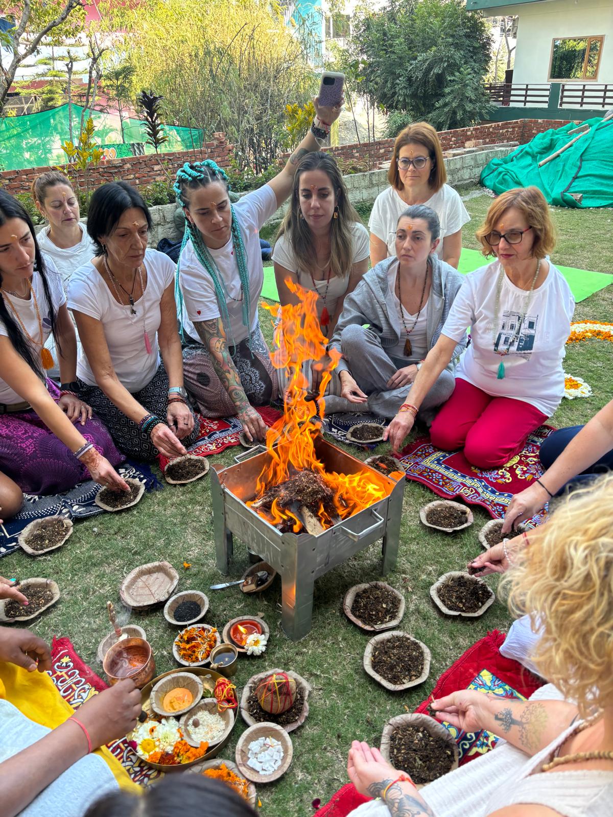 Un grupo medita en círculo alrededor de un fuego ritual, con ofrendas y flores en un jardín.