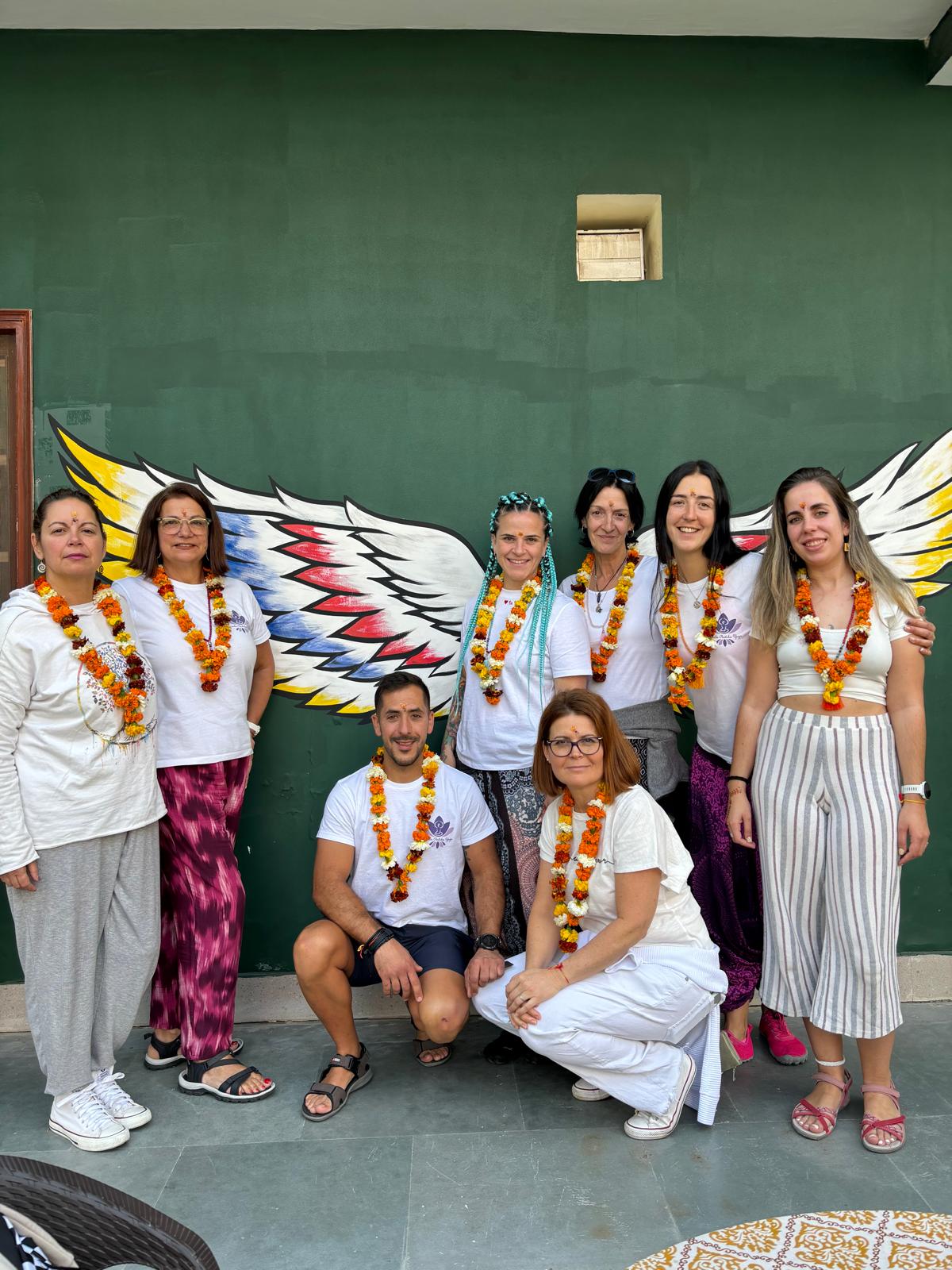 Grupo de viajeros posando con guirnaldas de flores frente a un mural de alas en India.