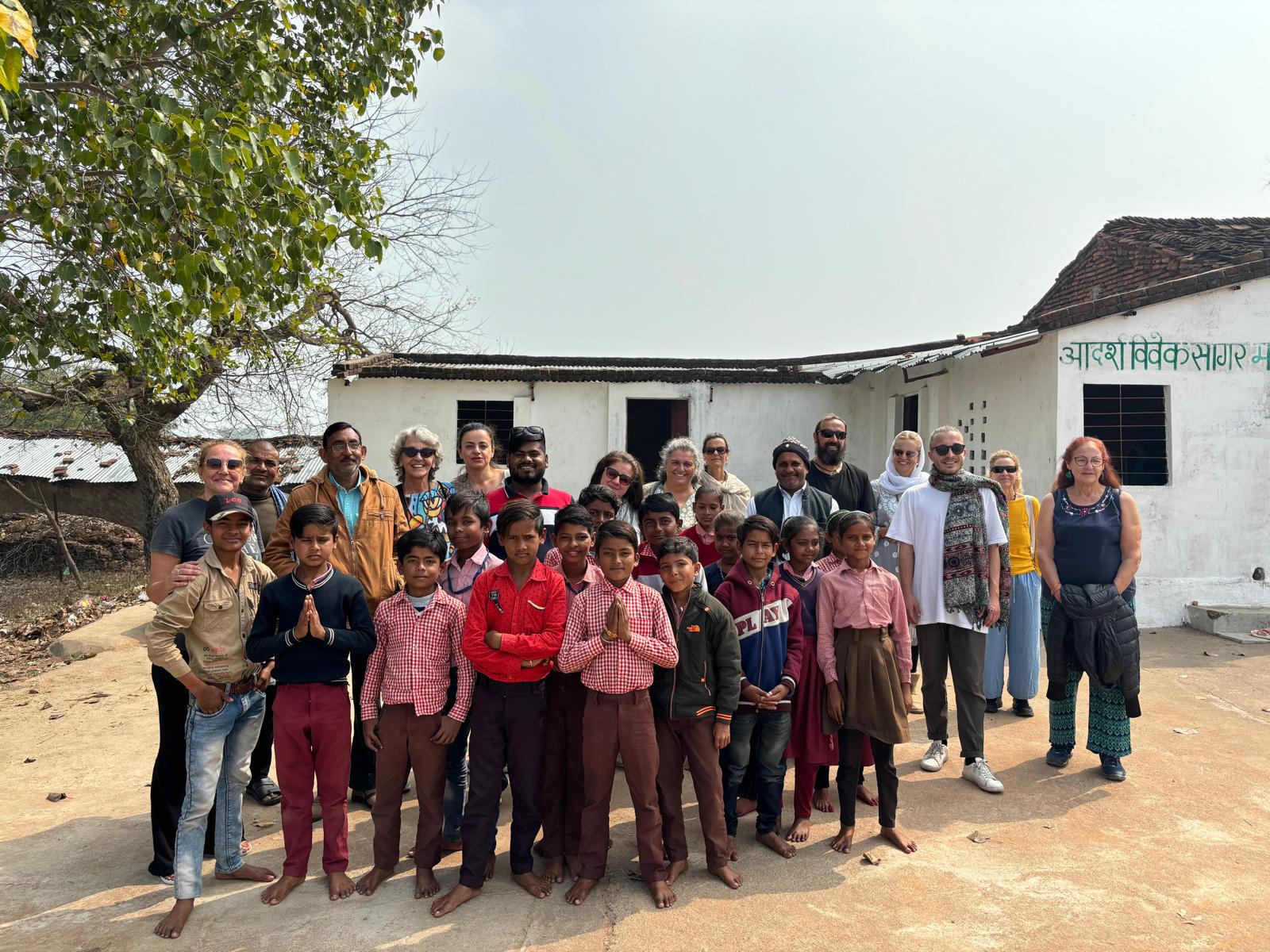 Un grupo de viajeros visita una comunidad rural, rodeados de niños, en un entorno sencillo y acogedor.