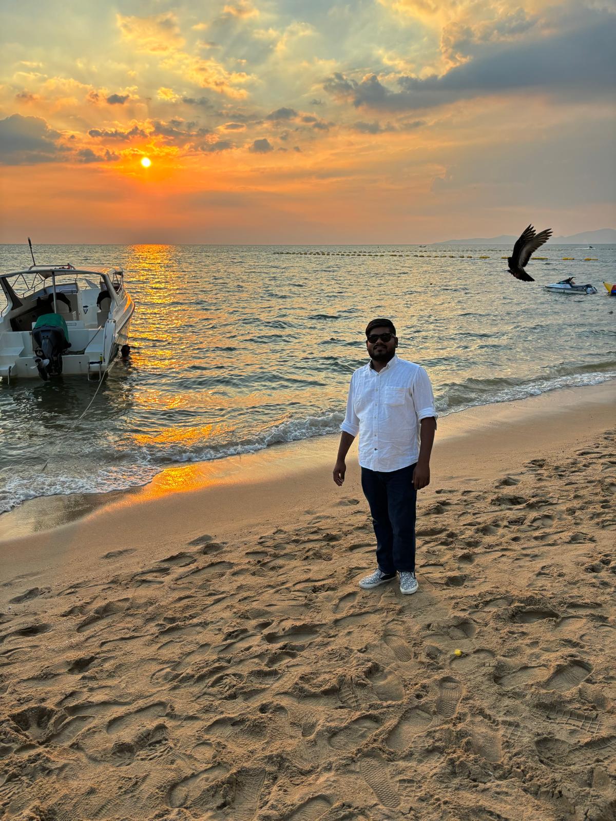 Sachin Rajak en la playa al atardecer con un barco tradicional, mostrando la belleza costera de India.